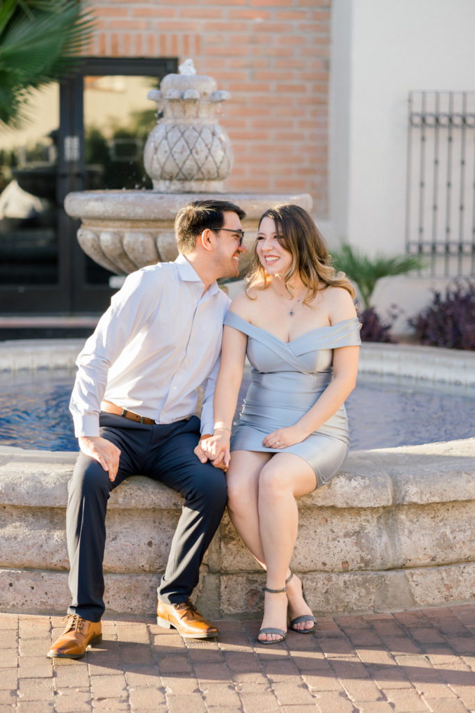 engagement couple sitting by a fountain at casas adobes plaza