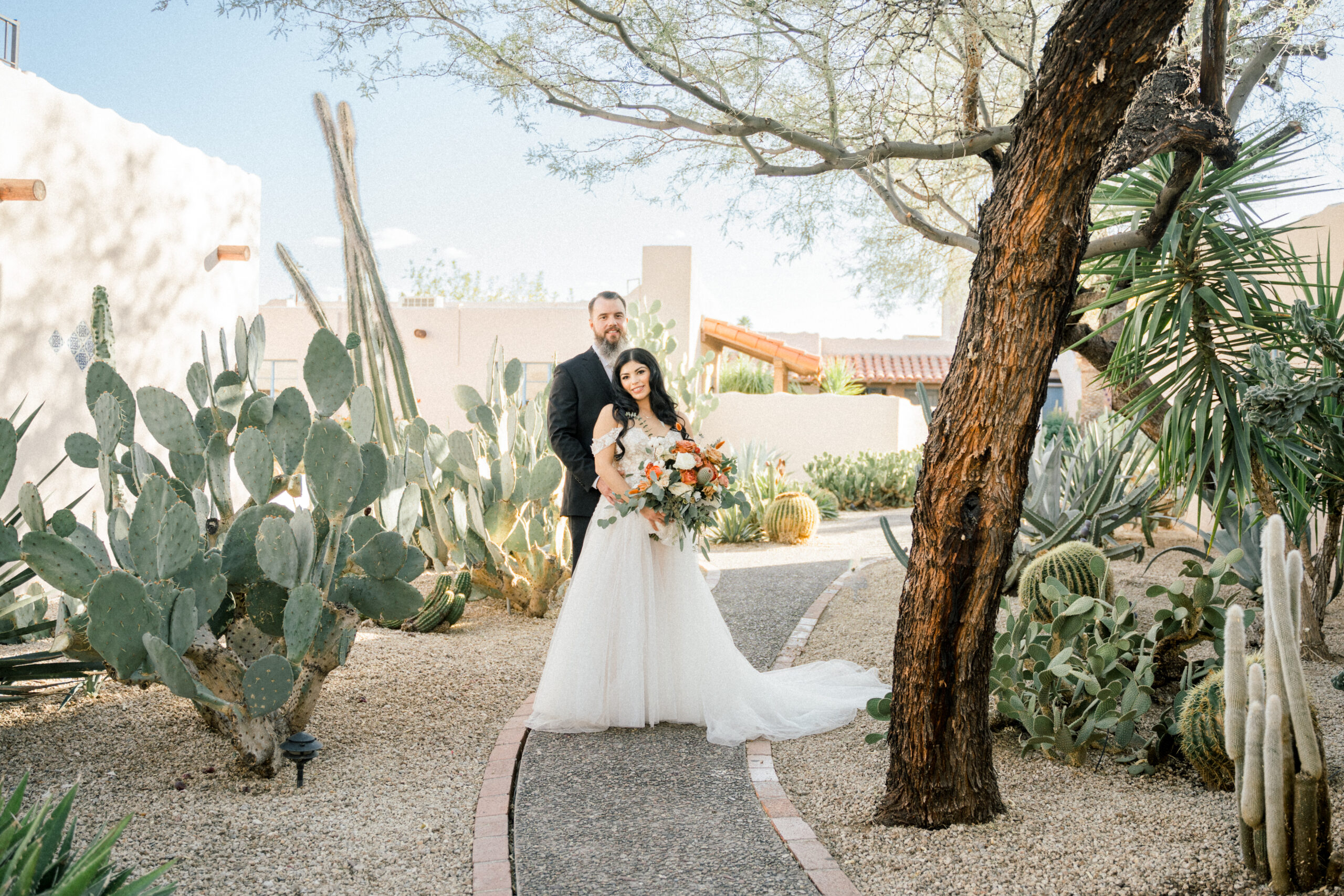 Desert Wedding in Tucson, Az. Bride and Groom posing by a walkway of native Arizona desert plants. Ruby Sandoval Photography.