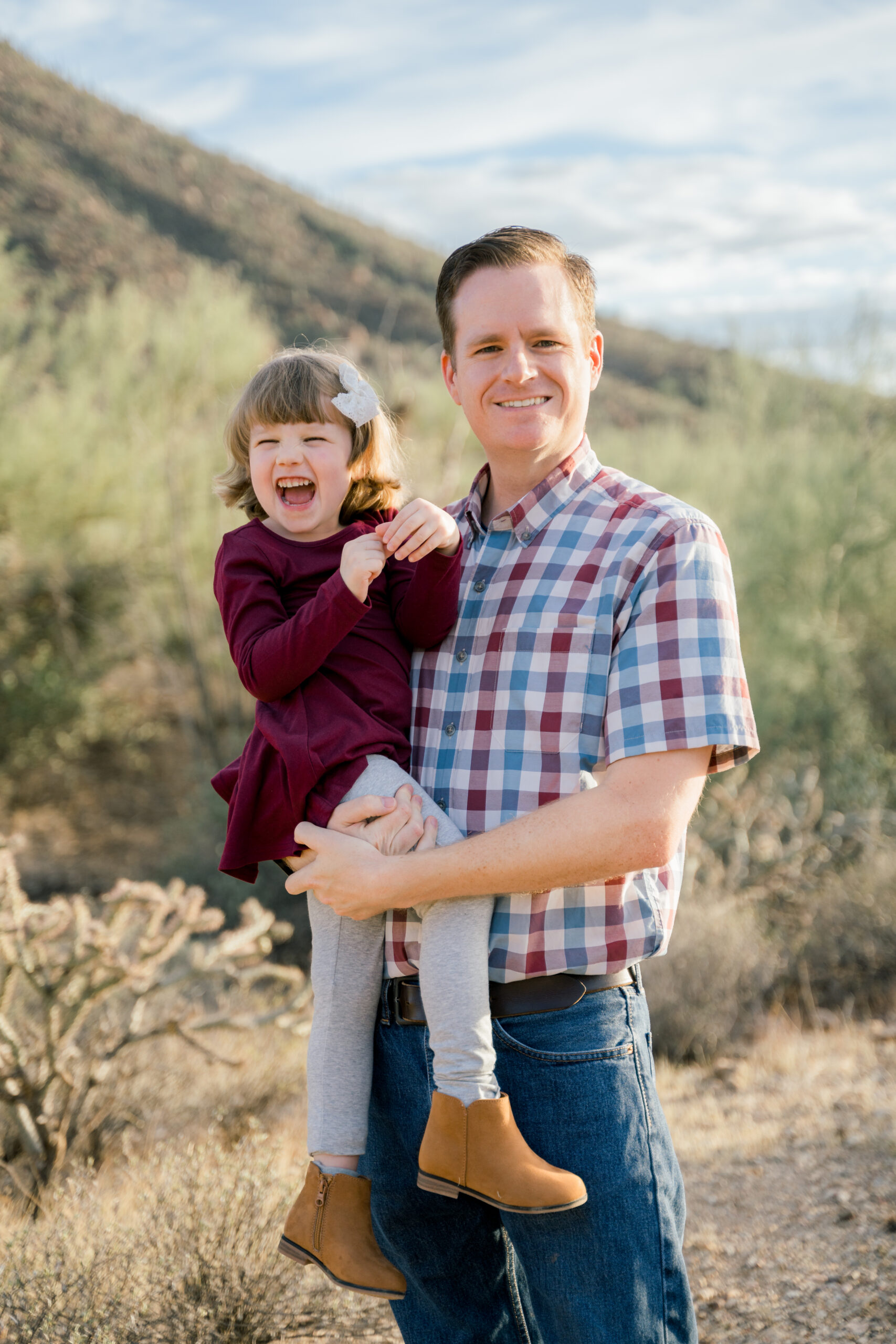 Dad and daughter poses in front of mountains during a family session at Gates Pass in Tucson, AZ. Ruby Sandoval Photography