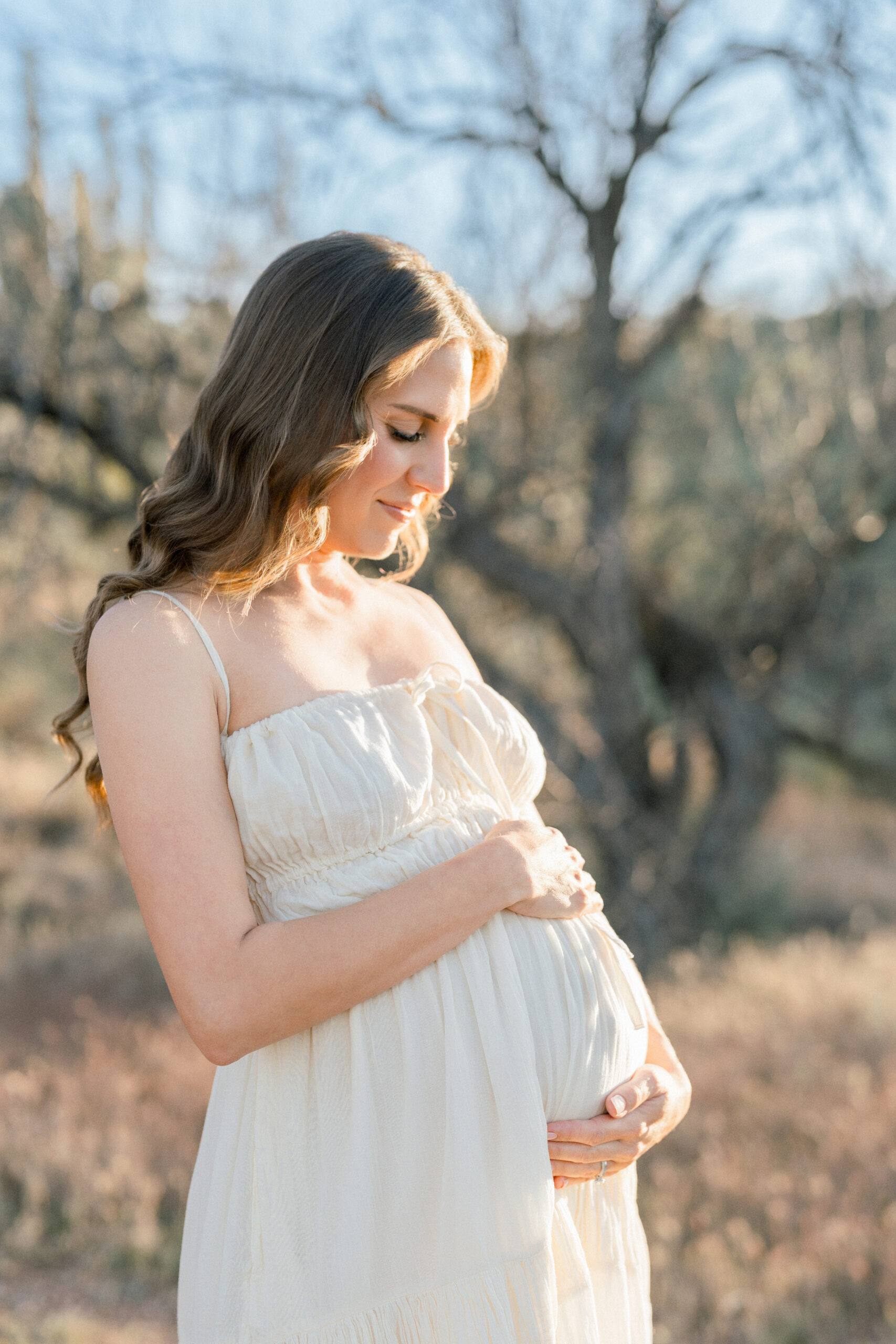 Pregnant mom holding belly while wearing a neutral toned dress during her Arizona maternity session